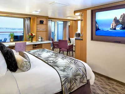 Blick in eine barrierefreie Neptune Suite an Bord der Zuiderdam mit großem Bett, Sitzecke und Meerblick durch die Fenster.