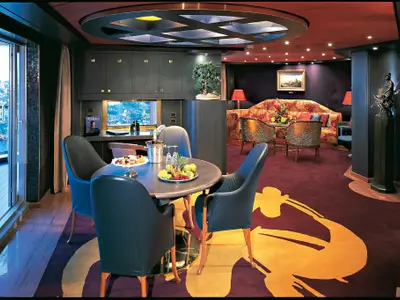 Blick in die großzügige Pinnacle Suite an Bord der Zuiderdam mit rundem Esstisch, stilvollem Sitzbereich, Kunstwerken und Balkontür.