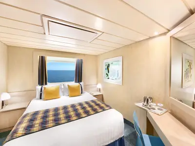 Eine helle und gemütliche Aussenkabine an Bord der MSC Armonia mit einem Doppelbett, zwei Nachttischen und Lampen. Ein grosses Fenster bietet einen weiten Blick auf das offene Meer. Gegenüber dem Bett befindet sich ein Schreibtisch mit Spiegel und einer Ablage für Getränke.