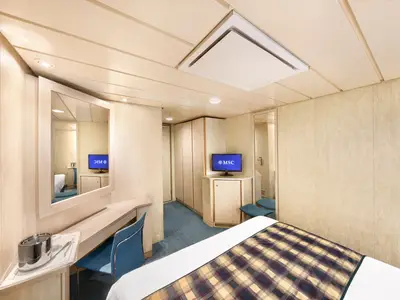 Blick in eine helle Aussenkabine der MSC Armonia mit Holzvertäfelung und blauen Akzenten. Ein Bett mit karierter Decke, ein Schreibtisch mit Stuhl, ein Fernseher und Schränke sind zu sehen.