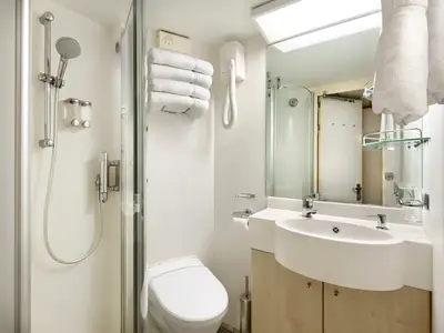 Dieses Pressefoto zeigt ein helles Badezimmer in einer Balkonkabine der MSC Armonia. Zu sehen sind eine Duschkabine mit verstellbarem Duschkopf, ein WC, ein Waschbecken mit Armatur und Seifenspender sowie ein Spiegel. Weiße Handtücher hängen an der Wand und über dem Spiegel. Ein Fön ist ebenfalls montiert.