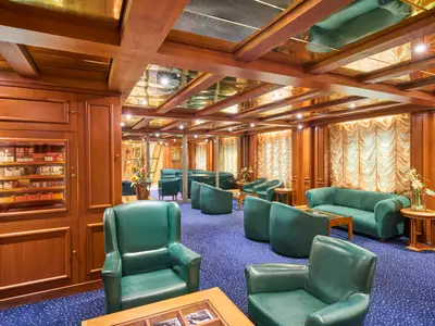 Ein luxuriöser Raum an Bord der MSC Armonia mit blauer Teppichboden, dunkelgrünen Ledersesseln und Sofas. Holzvertäfelungen und ein Humidor mit Zigarren sind sichtbar. Die Decke ist mit Holz und Spiegeln gestaltet.