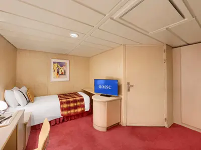 Innenansicht einer barrierefreien Kabine auf der MSC Armonia. Zu sehen ist ein Einzelbett mit weißer Bettwäsche und karierter Decke, ein kleiner Schreibtisch und ein Fernseher mit dem MSC-Logo. Der Raum hat helle Holzpaneele an den Wänden und einen roten Teppichboden.