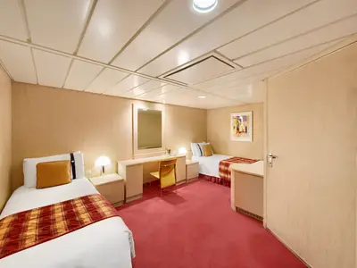 Innenansicht einer geräumigen, barrierefreien Kabine an Bord der MSC Armonia. Sie zeigt zwei Einzelbetten mit roten und gelben Tagesdecken, einen Schreibtisch mit Stuhl und einen großen Spiegel. Der Boden ist mit einem roten Teppich ausgelegt, die Wände sind hellbraun. Eine helle Decke mit Paneelen und integrierter Beleuchtung ist zu sehen.