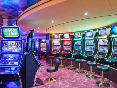 Blick in eine Spielhalle auf der MSC Armonia mit Reihen von beleuchteten Slot-Maschinen. Im Vordergrund stehen Barhocker bereit. Die Bildschirme der Maschinen zeigen bunte Grafiken und Jackpot-Anzeigen.