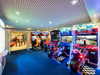 Ein gut beleuchteter Arcade-Spielbereich an Bord der MSC Armonia mit mehreren Rennsimulatoren für Autos und Motorräder auf blauem Teppich. Im Hintergrund ist ein Raum mit einem Billardtisch zu sehen.
