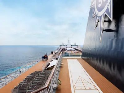 Blick von der Seite des Decks der MSC Armonia, mit Passagieren, die am Geländer stehen und auf das offene Meer blicken. Ein Shuffleboard-Feld ist auf dem Deck zu sehen.