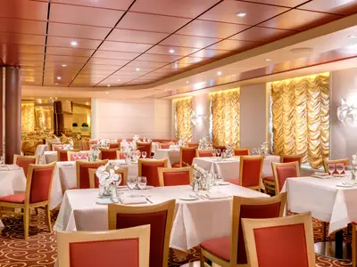 Elegantes Restaurant Marco Polo an Bord der MSC Armonia mit festlich gedeckten Tischen und roten Stuehlen. Der helle Raum ist mit goldenen Vorhaengen und stilvollen Leuchten ausgestattet.
