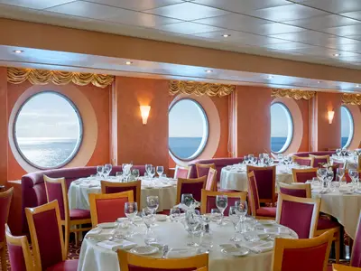 Blick in das Marco Polo Restaurant an Bord der MSC Armonia mit gedeckten Tischen, roten Stühlen und runden Fenstern, die einen weiten Meerblick bieten.
