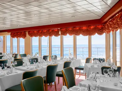Elegantes Restaurant La Pergola an Bord der MSC Armonia. Fein gedeckte Tische mit weißen Decken und dunkelgrünen Stühlen, dazu Meerblick durch große Panoramafenster.