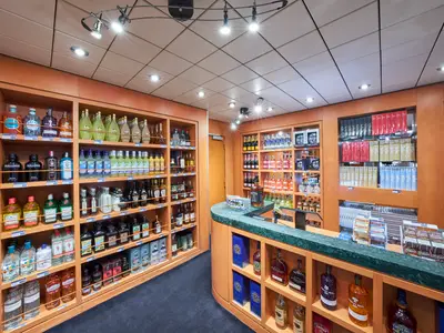 Ein gut beleuchteter Duty-Free-Shop mit Regalen voller Spirituosen, Weine und Tabakwaren an Bord der MSC Armonia. Eine grüne Marmortheke prägt den Vordergrund.