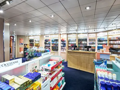 Heller, moderner Duty-Free-Shop an Bord der MSC Armonia. Regale voller Parfüms und Kosmetika von Marken wie L'Occitane und Lancôme. Eine Holzkasse und helle Deckenbeleuchtung sind zentral sichtbar.