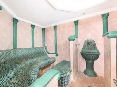 Blick in ein Dampfbad an Bord der MSC Armonia. Es zeigt grüne, mit kleinen Kacheln bedeckte Sitzbänke, mehrere grüne Ziersäulen und einen passenden Wandbrunnen vor rosa gefliesten Wänden.