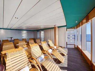 Ein heller Entspannungsraum im MSC Aurea Spa der MSC Armonia mit Reihen von Holzliegen. Große Fenster bieten einen weiten Blick auf das offene Meer.