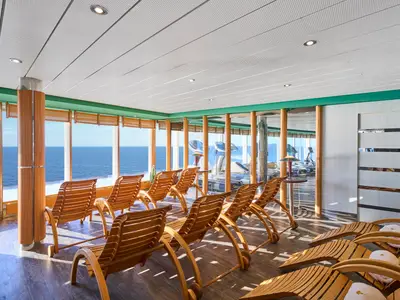 Ein heller Entspannungsraum im MSC Aurea Spa an Bord der MSC Armonia mit Reihen von Holzliegen. Große Fenster bieten einen weiten Blick auf das offene Meer.