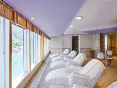 MSC Aurea Spa der MSC Armonia: Weisse Mosaik-Liegen vor Panoramafenstern mit Meer- und Küstenblick. Bunte Mosaikwände, Handtücher.