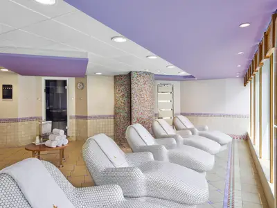Entspannungsbereich im MSC Aurea Spa der MSC Armonia. Helle Liegen, Fliesenboden, Mosaik-Säulen und violette Decke. Fensterfront rechts.