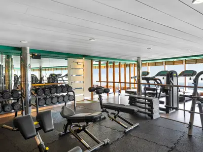 Ein heller Fitnessbereich an Bord der MSC Armonia mit Technogym-Laufbaendern, Hantelstaendern und Bänken. Grosse Fenster bieten einen weiten Blick auf das offene Meer.