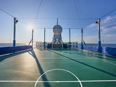 Sonniges Sportfeld an Bord der MSC Armonia auf dem Oberdeck. Basketballkorb, Fussballtor, Spielfeldlinien. Lange Schatten fallen aufs Feld. Meer im Hintergrund.