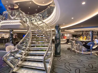 Das luxuriöse Infinity Atrium der MSC Bellissima mit einer glitzernden Swarovski-Treppe. Rechts eine moderne Bar mit Hockern. Elegant und einladend.