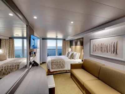 Moderne Balkonkabine an Bord der MSC Bellissima. Großes Doppelbett, Balkon mit Meerblick, Sofa, TV und Wandkunst in warmen Farben.