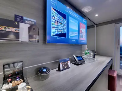 Moderne Balkonkabine an Bord der MSC Bellissima. Ein Schreibtisch mit Smart-TV, digitalem Assistenten, Telefon und Kaffeemaschine. Balkontür mit Meerblick.