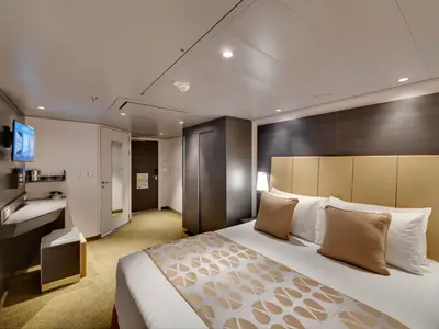 Innenansicht einer geräumigen, barrierefreien Balkonkabine an Bord der MSC Bellissima. Sie zeigt ein großes Doppelbett, einen Schreibtisch mit TV und einen Kleiderschrank in modernem Design.