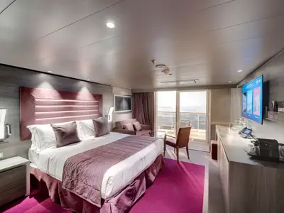 Helle, geräumige Balkonsuite an Bord der MSC Bellissima. Die barrierefreie Kabine zeigt ein Doppelbett, Sofa, Schreibtisch mit TV und Balkon mit Meerblick.
