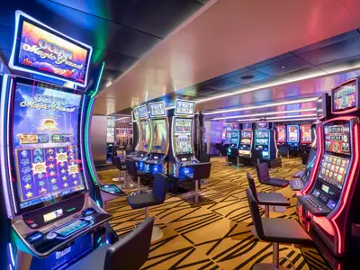 Blick in das modern beleuchtete Imperial Casino an Bord der MSC Bellissima mit Reihen von bunten Spielautomaten und leeren Barhockern auf gemustertem Teppichboden.