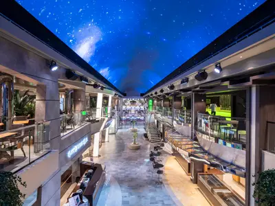Die moderne Galleria Bellissima auf der MSC Bellissima. Eine lange Innenpromenade mit Bars, Geschäften und Sitzbereichen. LED-Sternenhimmel. Elegant.