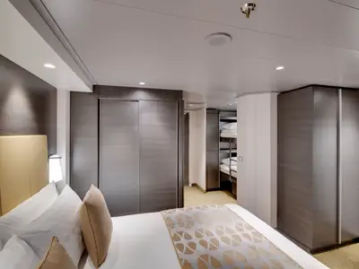 Moderne Familienkabine an Bord der MSC Bellissima mit Doppelbett, holzfarbenen Schränken und einem Bereich mit Etagenbetten. Warme Beleuchtung und helles Interieur dominieren.