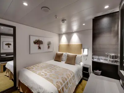 Moderne und helle Innenkabine an Bord der MSC Bellissima. Zu sehen sind ein Doppelbett, ein großer Spiegel, ein Schreibtischbereich und Regale mit Gläsern. Der Raum ist funktional und elegant gestaltet.