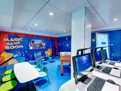 Kinderbereich an Bord der MSC Bellissima. Bunte Wandbilder mit Sternen und "Magic Game Room" Schriftzug. Mit Computern, einem Tischkicker, Tischen und Stühlen für Kinderaktivitäten.