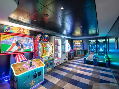 Ein lebhafter Arcade-Spielebereich an Bord der MSC Bellissima, ausgestattet mit hell beleuchteten Videospielautomaten, Skee-Ball-Spielen und einem Preis-Hub, bereit für Spieler jeden Alters. Der Raum ist modern gestaltet mit blauer Beleuchtung und gemustertem Teppich.