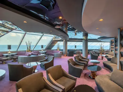 Die luxuriöse Top Sail Lounge an Bord der MSC Bellissima. Helle Einrichtung, bequeme Sessel und Sofas mit Blick auf das weite Meer durch grosse Fenster.