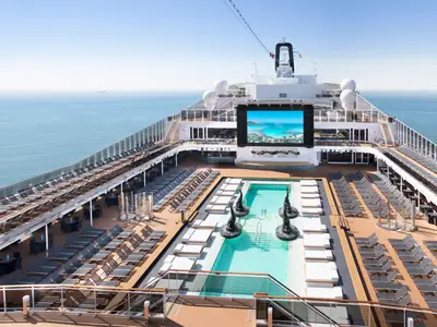 Blick auf das Atmosphere Pool Deck der MSC Bellissima. Hunderte Liegestühle umrunden den Pool mit Wassersäulen. Eine große LED-Leinwand und das offene Meer prägen die Szene.