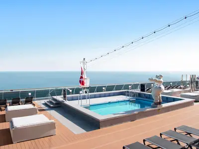 Die MSC Bellissima zeigt ihren Horizon Pool auf dem Oberdeck mit Meerblick. Eine weiße Skulptur steht neben dem Pool, im Hintergrund weht eine rote Flagge.