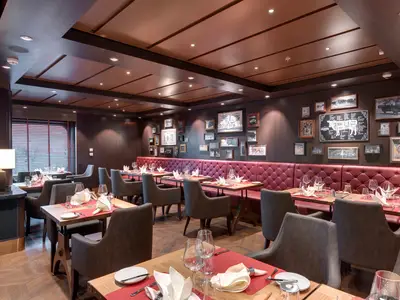 Spezialitätenrestaurant "Butcher's Cut" auf der MSC Bellissima. Rote Lederbänke, dunkle Holzwände mit Bildern von Rindern und Fleischschnitten. Elegant gedeckte Tische, warmes Licht.