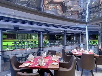 Innenansicht des modernen Spezialitätenrestaurants Kaito an Bord der MSC Bellissima. Gedeckte Tische, darunter eine grün beleuchtete Bar, reflektierende Decke.