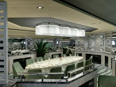 Blick in das elegant gestaltete Posidonia Restaurant an Bord der MSC Bellissima mit zahlreichen gedeckten Tischen. Die Einrichtung ist modern mit grünen Stühlen, einer großen Lichtinstallation und reflektierenden Oberflächen.