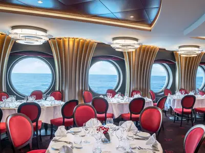 Blick in das Il Ciliegio Restaurant an Bord der MSC Bellissima. Elegante Tische mit roten Stühlen und runden Fenstern bieten weiten Meerblick.