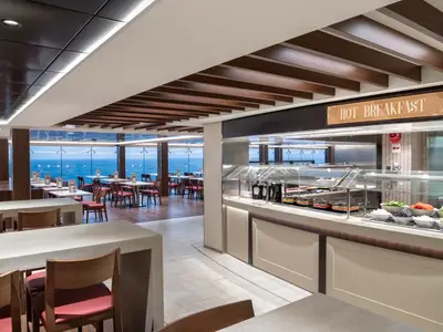 Das helle Marketplace Buffet Restaurant an Bord der MSC Bellissima. Eine Hot Breakfast-Theke und Salatbar. Moderne Sitzbereiche mit Meerblick durch Panoramafenster.