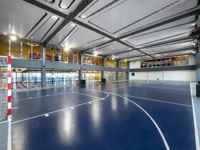 Ein großer Sportplex an Bord der MSC Bellissima mit blauem Spielfeld, weißen Linien für Basketball und Futsal sowie zwei Toren. Modernes Design mit Glasfassaden.