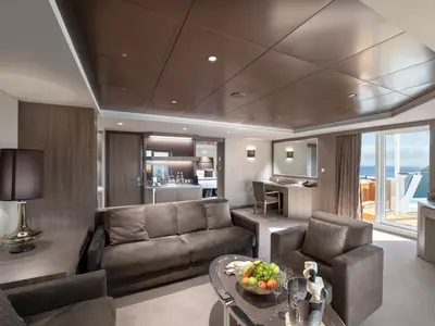 Ein weitläufiger Wohnbereich in einer luxuriösen Yacht Club Royal Suite an Bord der MSC Bellissima mit Sofa, Sesseln, Minibar, Schreibtisch und einem Balkon mit Meerblick.