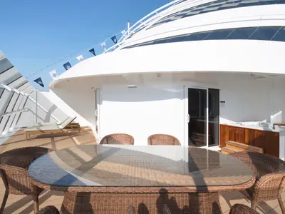 Blick auf die private Terrasse einer Yacht Club Royal Suite an Bord der MSC Bellissima, ausgestattet mit einem Esstisch, Korbstühlen, Sonnenliegen und einem Whirlpool.
