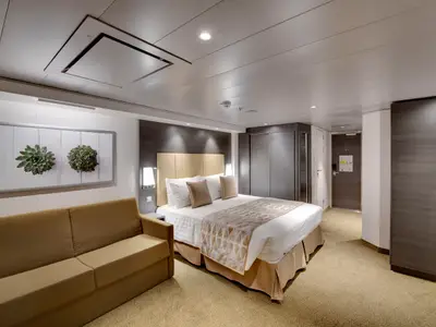 Eine helle und geräumige Premium Suite Aurea an Bord der MSC Bellissima mit Doppelbett, beigem Sofa und moderner Einrichtung. An der Wand hängt ein Bild mit Pflanzenmotiven.