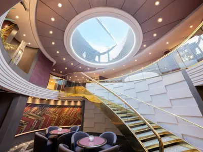Das stilvolle Atrium der MSC Divina zeigt eine goldene Wendeltreppe, ein großes rundes Oberlicht und eine moderne Lounge mit Sitzgelegenheiten und Kunstwerken.