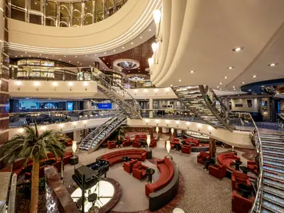 Das weitläufige, elegant beleuchtete Atrium der MSC Divina erstreckt sich über mehrere Ebenen mit prunkvollen Treppen, roten Sofas und Lounges.