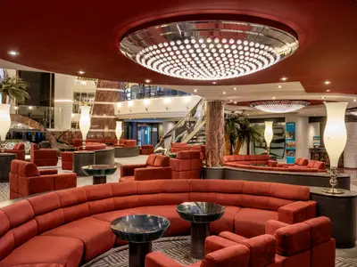 Das Atrium der MSC Divina bietet rote Sofas, Tische, grosse Kronleuchter und eine geschwungene Treppe. Palmen ergänzen das elegante Interieur an Bord.