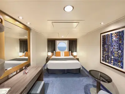 Moderne Aussenkabine an Bord der MSC Divina. Im Zentrum ein Doppelbett mit Bullauge und Meerblick. Links ein Waschtisch und Schreibtisch mit grossem Spiegel. Rechts ein abstraktes Kunstwerk und kleiner Beistelltisch. Blauer Teppichboden.